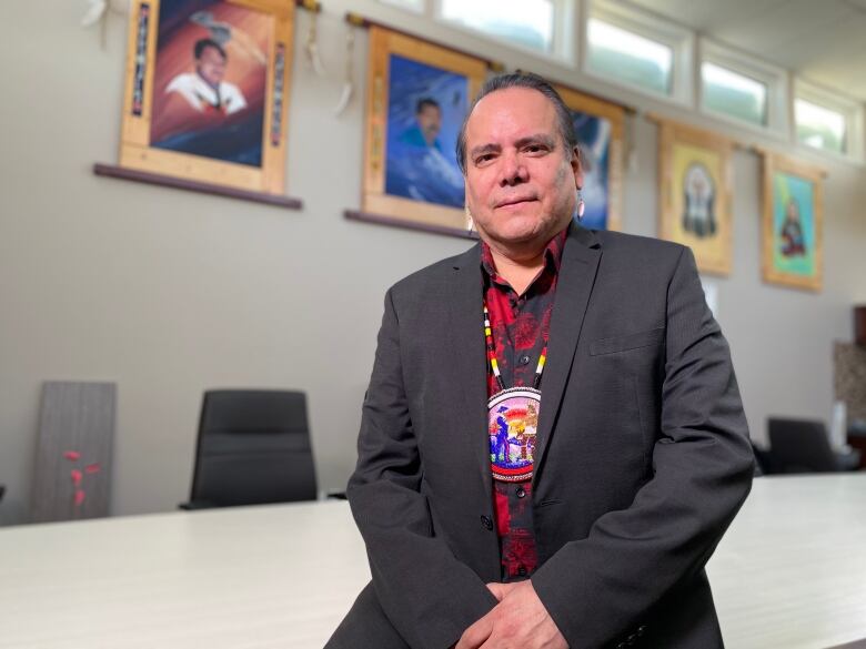 An Indigenous man sits wearing a beaded medallion and a suit.