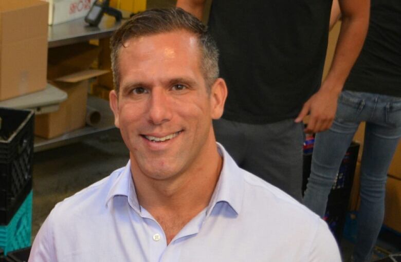 A smiling man with short hair. He is wearing a baby blue button up shirt.