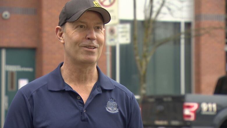 A white man wearing a police T-shirt smiles while outdoors.