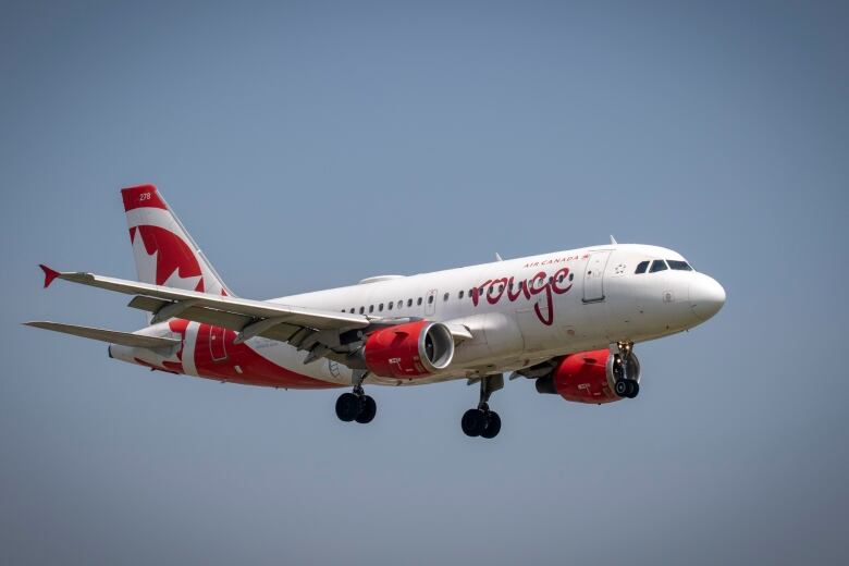 An Air Canada Rouge plane flies through the sky.