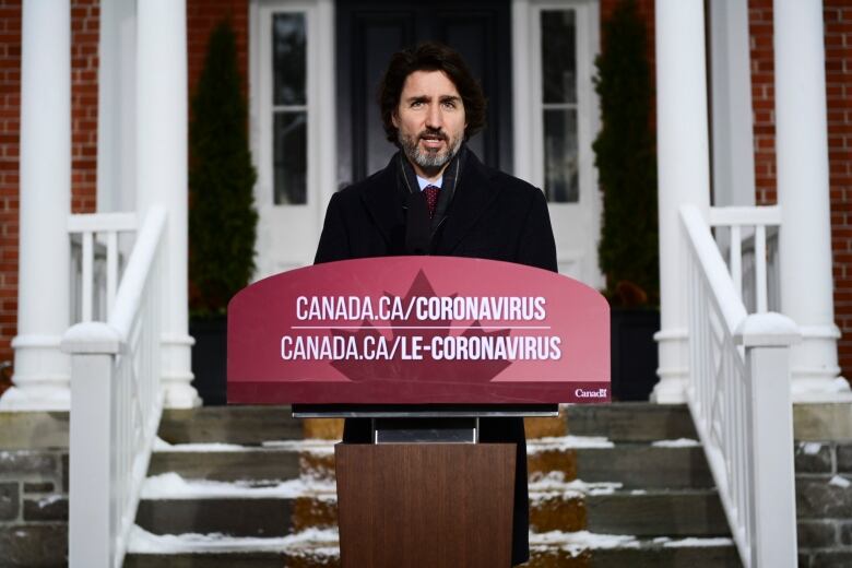 A bearded man speaks at a podium.