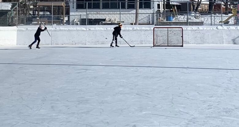 Two boys play hockey on an outdoor rink 