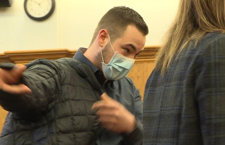 A younger man with cropped brown hair puts his arm in a black puffer jacket. 