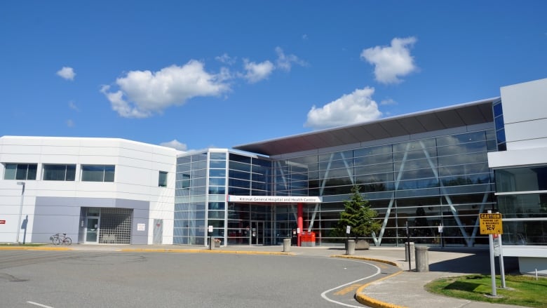 A long, low-slung white building in an L shape with a glass front and a large circular driveway.