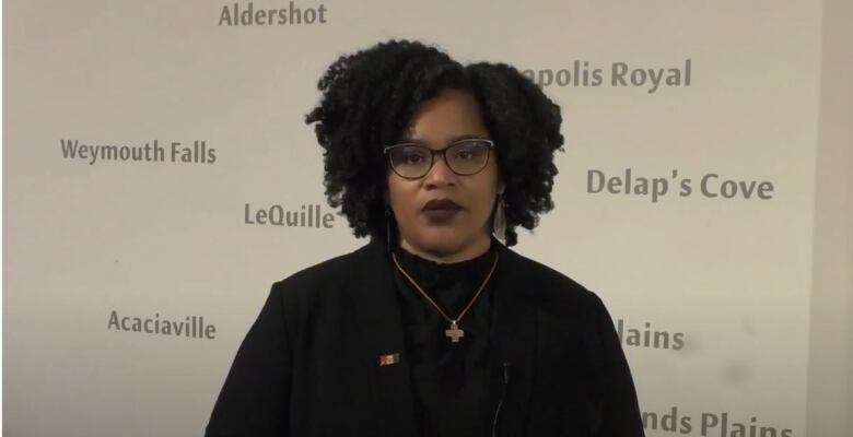 A Black woman with dark hair wearing a black turtleneck and blazer