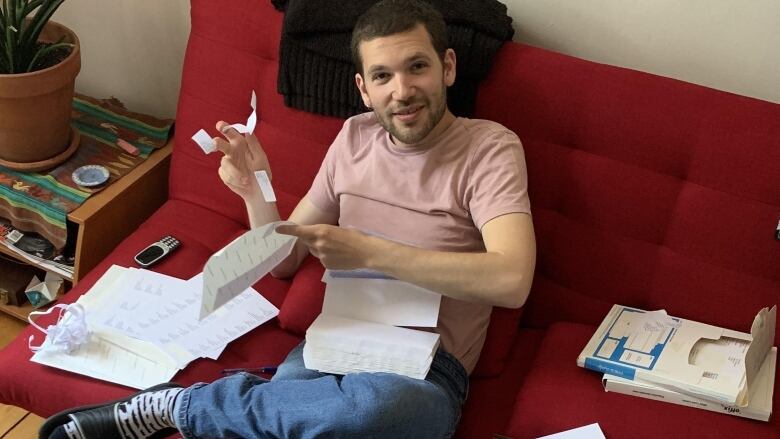 A man sits on a couch, surrounded by papers and letters.