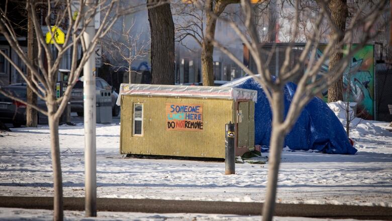 A picture of a small wooden shelter in a Toronto park that has a sign saying someone lives here.