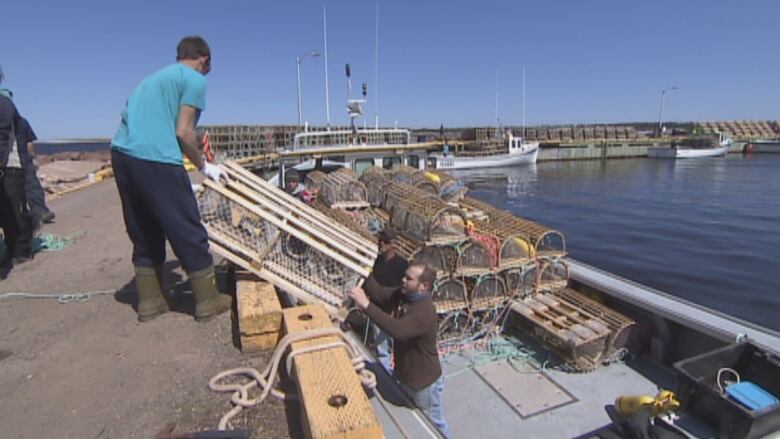 A man lowers a lobster trip to another man standing in a boat.