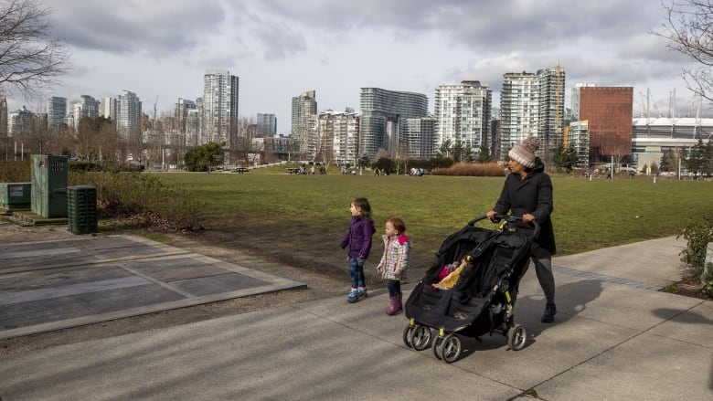 A woman is pushing a black stroller and beside her are two small kids in toques and jackets. 