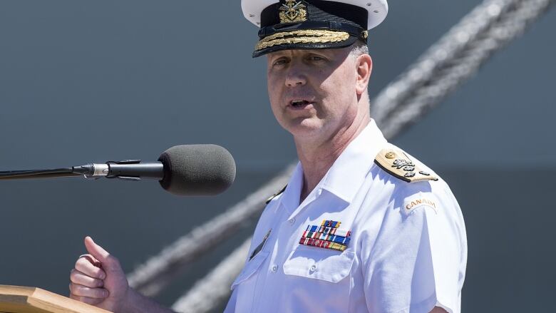 A man wearing a navy uniform speaks at a podium.