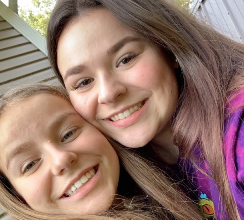 Two similar-looking girls smile at the camera with their cheeks pressed together. 