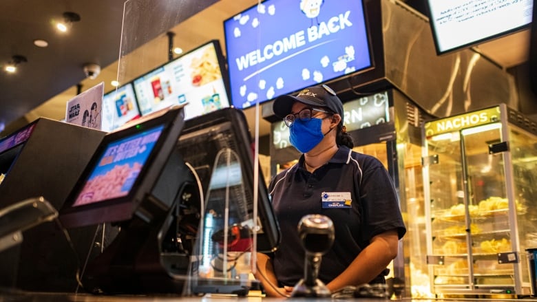 A person is scene waiting to serve customers behind the concession stand at a movie theatre.