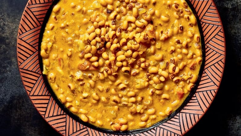 Overhead shot of a shallow bowl filled with kunde, black-eyed peas and tomatoes in peanut sauce. It sits on a dark grey surface. 