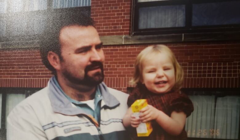 A dark-haired bearded man is holding a smiling, blond-haired child. 