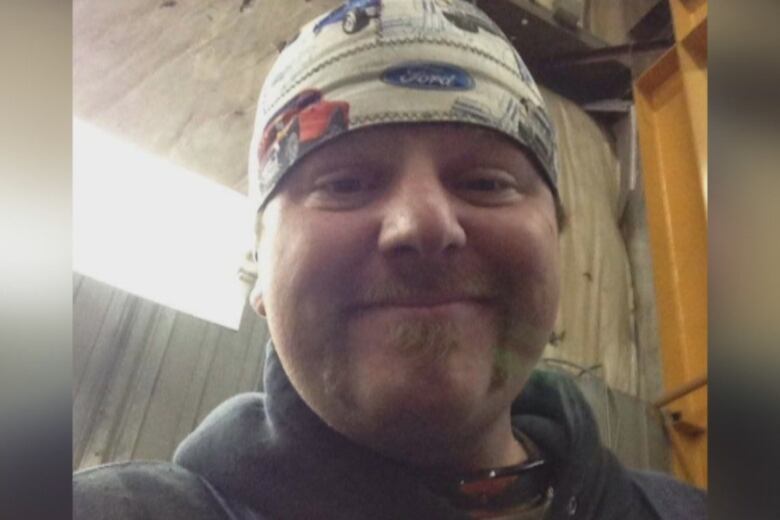 A man smiles while wearing a bandana around his head. 