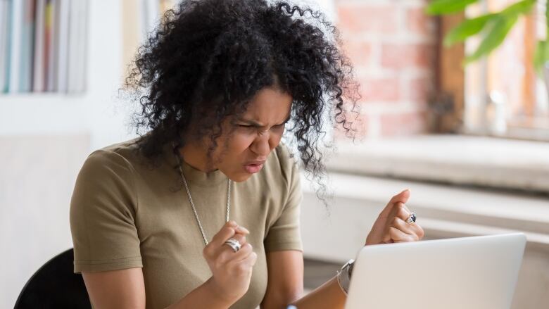 A Black woman gestures with her fists while sitting at a computer desk.