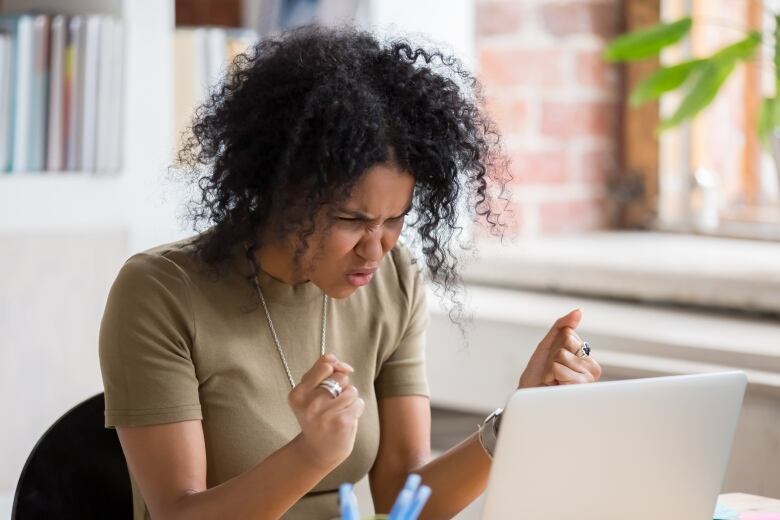 A Black woman gestures with her fists while sitting at a computer desk.