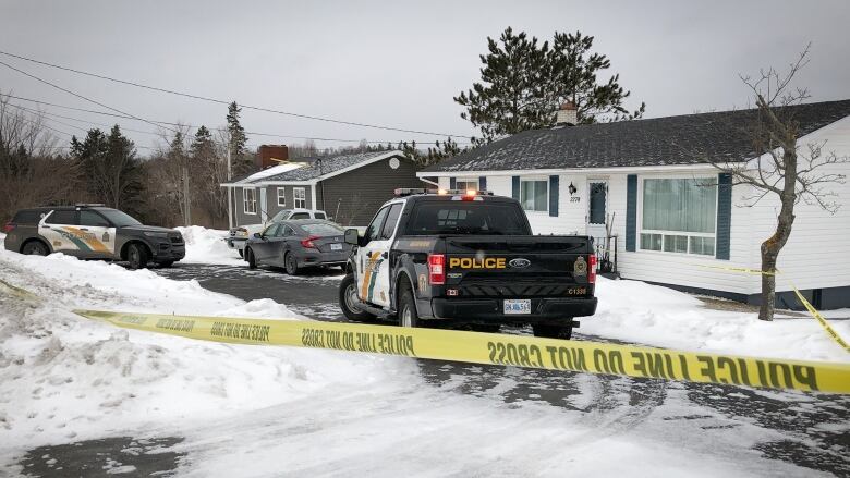 Yellow police tape blocks access to a home's driveway, which contains several police vehicles.