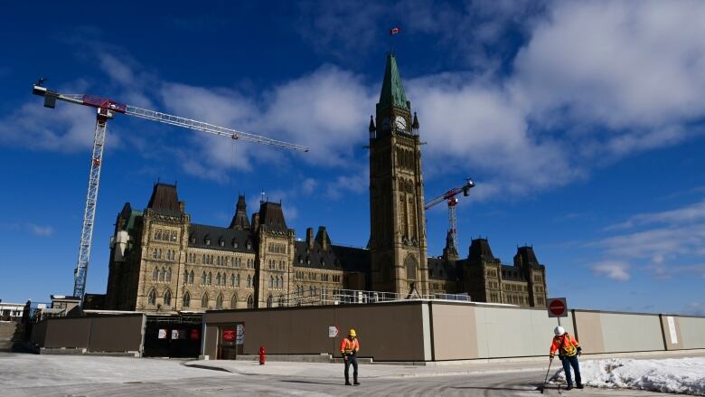 A large gothic building is surrounded by construction cranes under a blue sky.