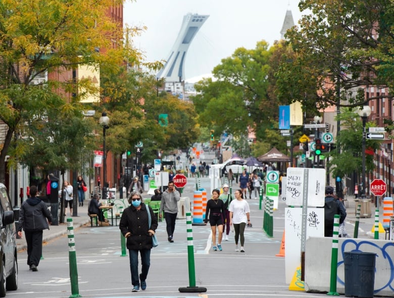 People wearing masks walk down a street in Montreal. Cars have been barred from the area with blockers.