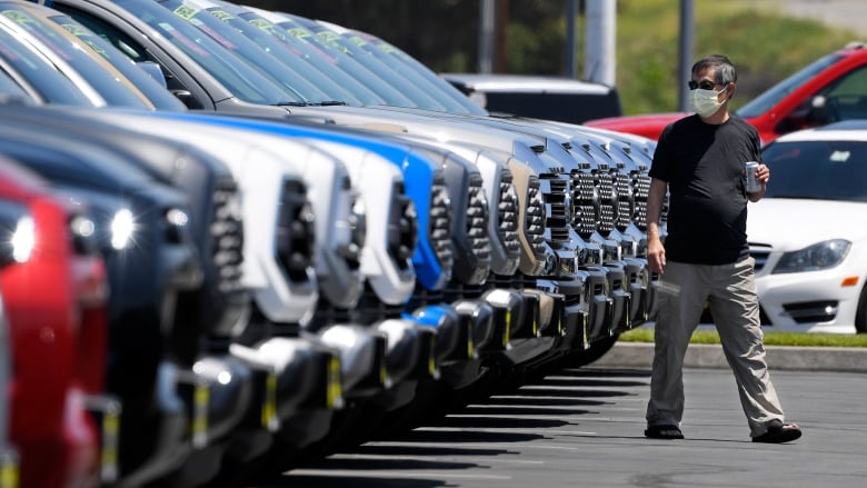 A man wearing a mask walks in front of a long row of trucks for sale.