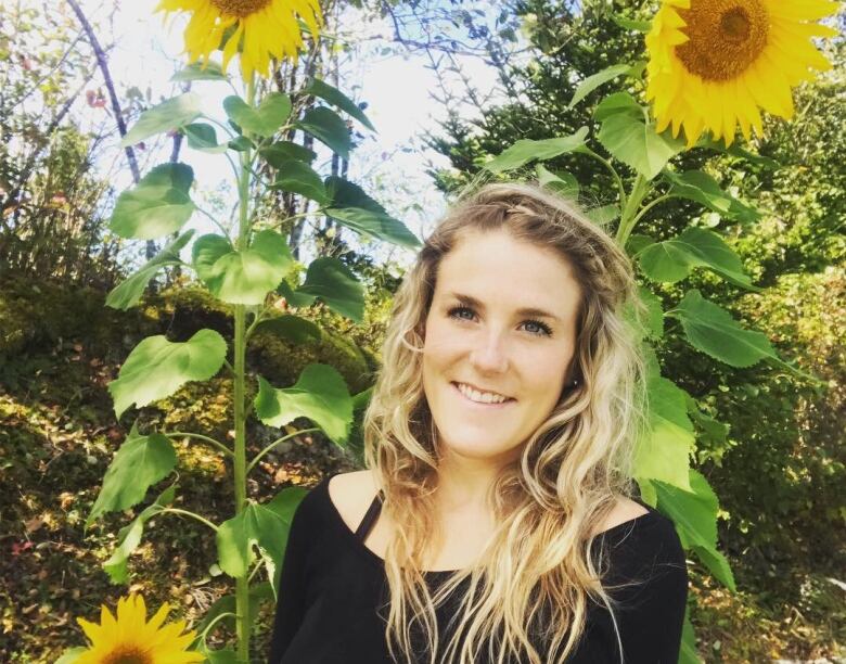 A smiling young woman surrounded by several sunflowers. 