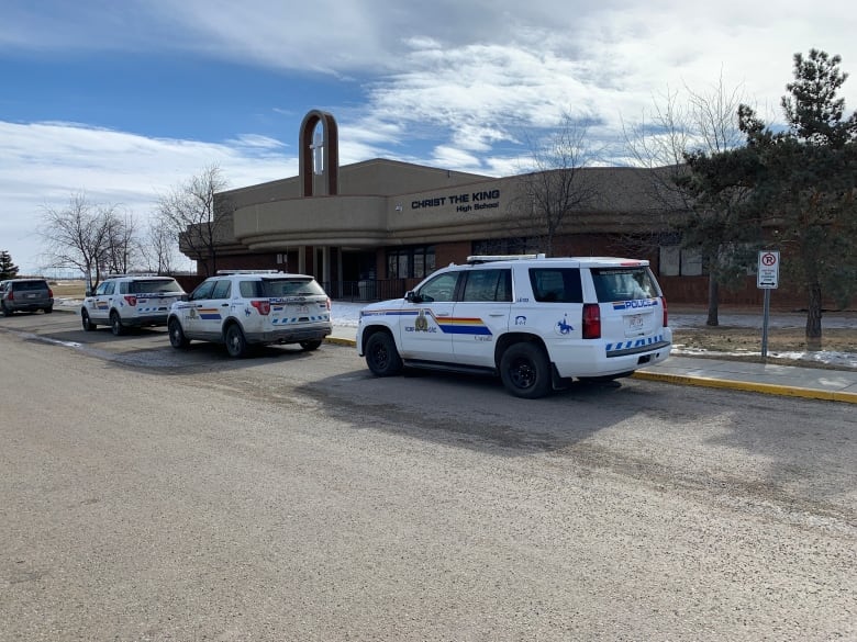 Police vehicles are lined up outside a brown building with a sign that says 