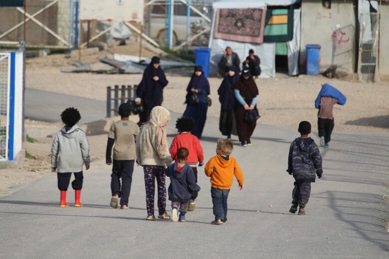 women and children seen from behind walking along an rural looking road