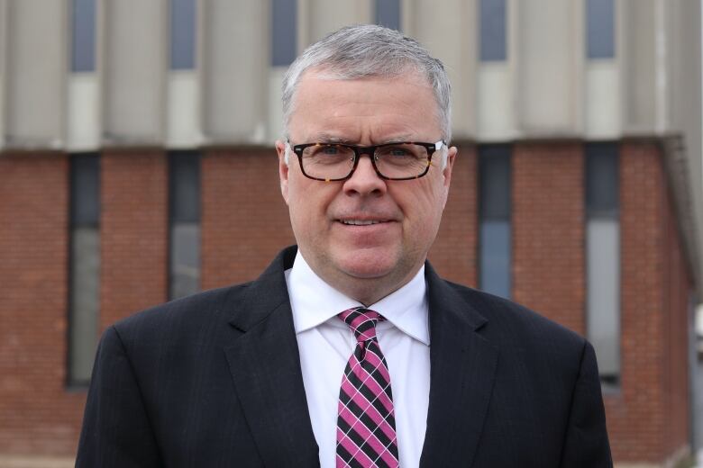 A man in a black suit wearing wearing glasses and with short grey hair.