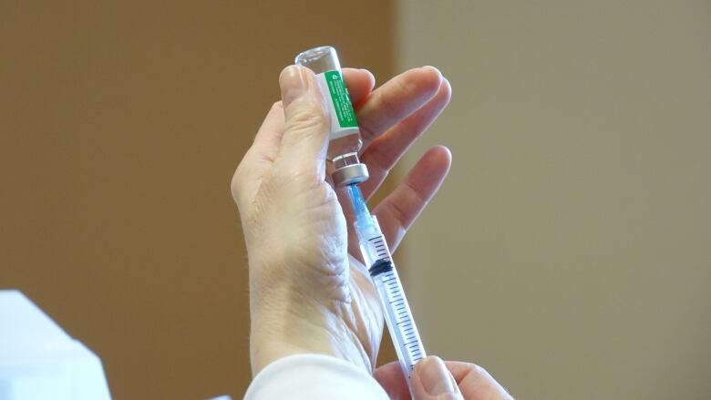 A closeup of hands inserting a syringe into a glass vaccine vial.