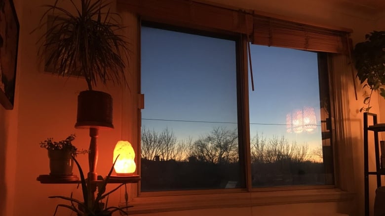 A photo of a window overlooking a snowy landscape while the sun is setting.