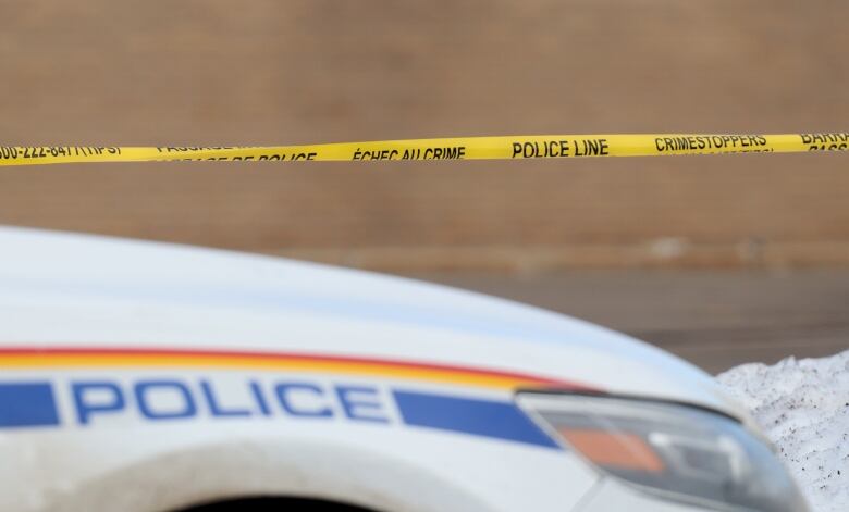 Yellow police tape stretches across the image with an RCMP cruiser in the foreground showing the work 