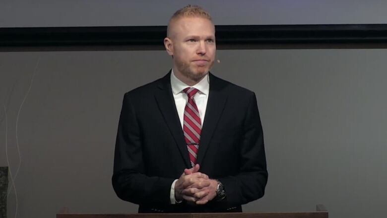 a man in a blue suit and red tie stands at a podium