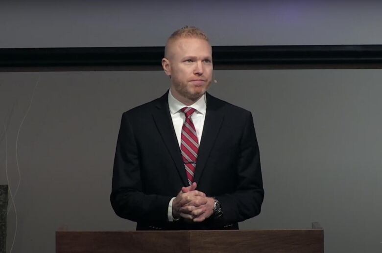 a man in a blue suit and red tie stands at a podium