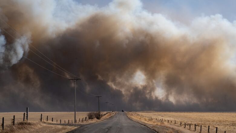 Smoke billows in the distance beyond a narrow highway.