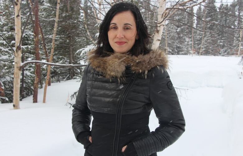 A woman who appears to be white standing outside in the snow with a black coat on.