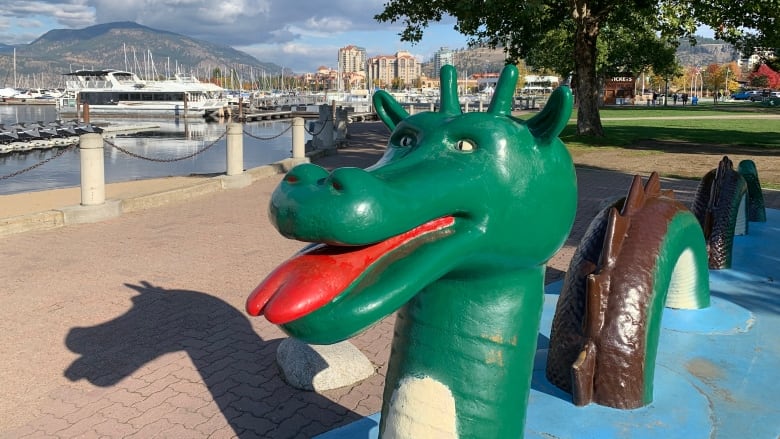 A green dragon-like statue is seen on the shore of a lake.