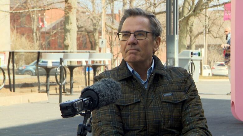 A man sitting in a wheelchair speaks into a microphone.