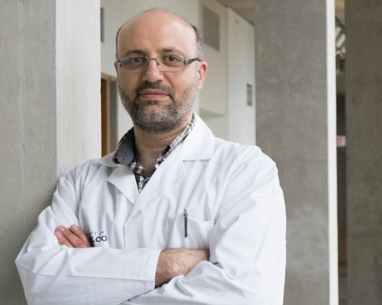 A man in a lab coat crosses his arms looking at the camera.