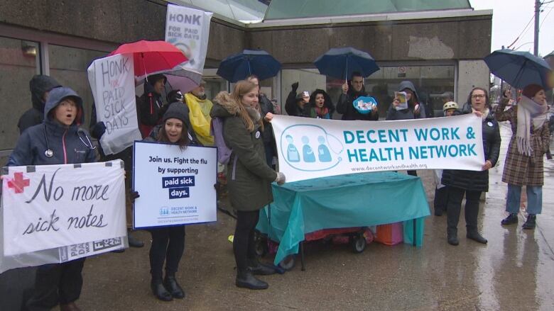 Protestors carry signs at a rally in support of paid sick days.