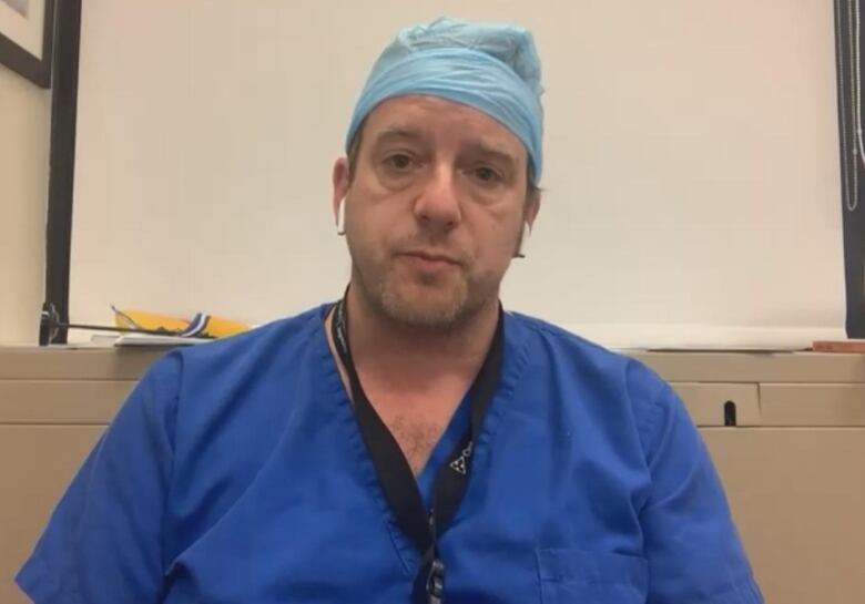 A webcam view of a frowning man in bright blue scrubs.