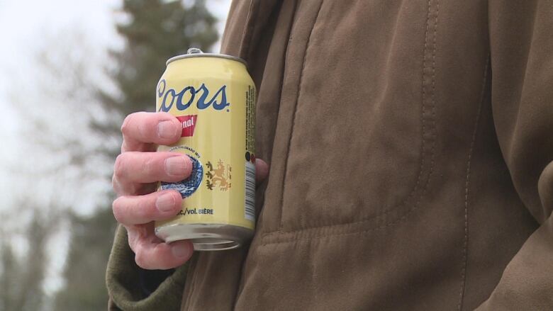 A person holds a yellow Coors beer can in their hand.