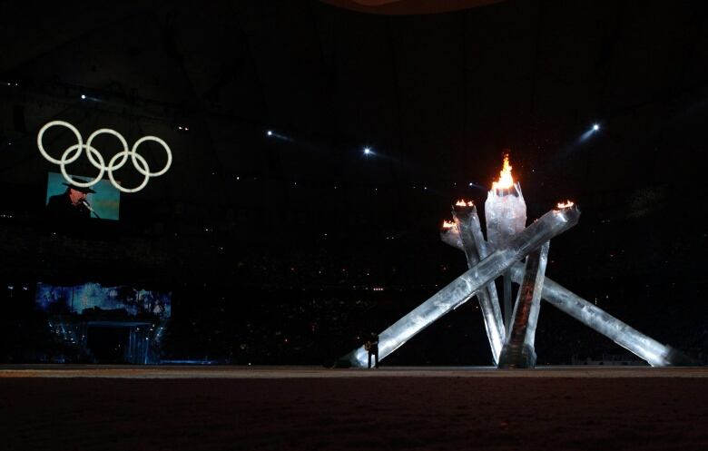 A large torch is seen burning with the Olympic rings in the background.