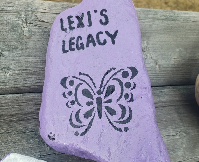 A flat rock painted purple with black lettering and a butterfly. 