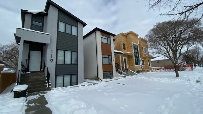 A row of large houses, one of which is under construction, are shown in winter.