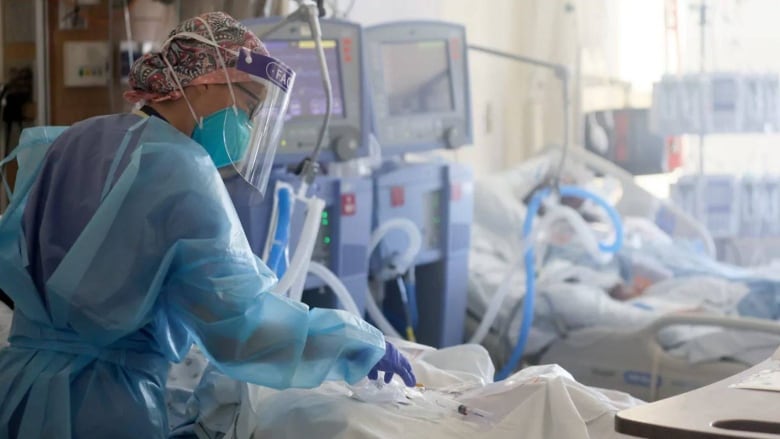 A nurse wearing full personal protective gear cares for COVID-19 patients in a hospital unit.