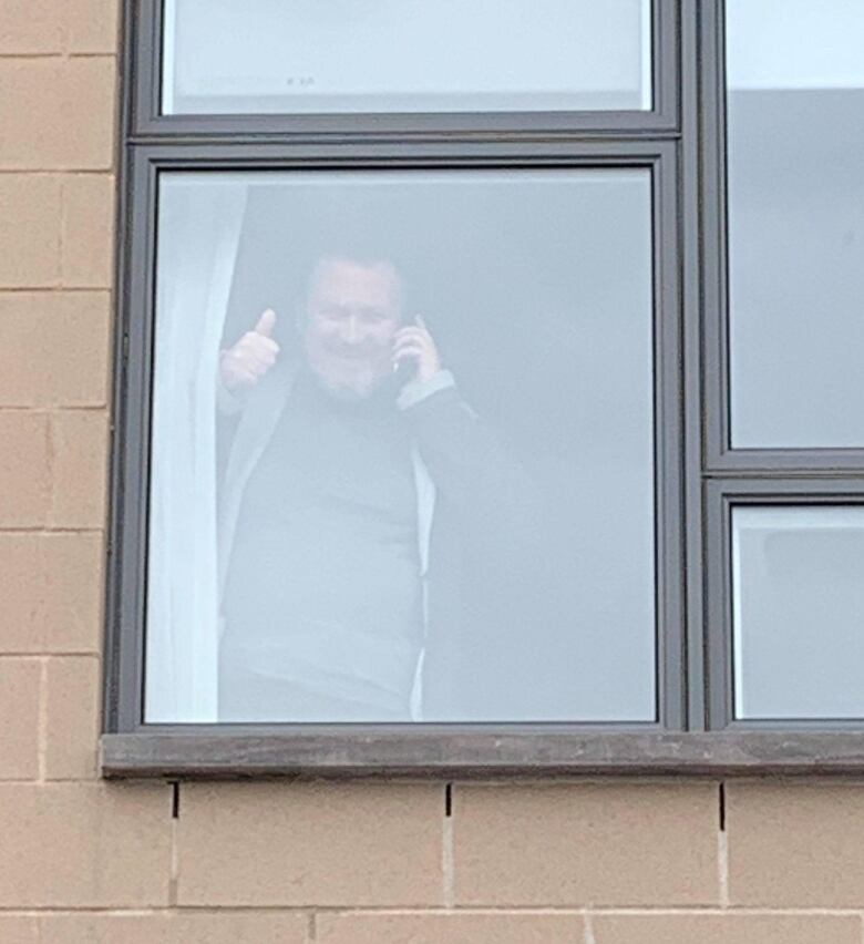 A man gives a thumbs up standing behind a window 