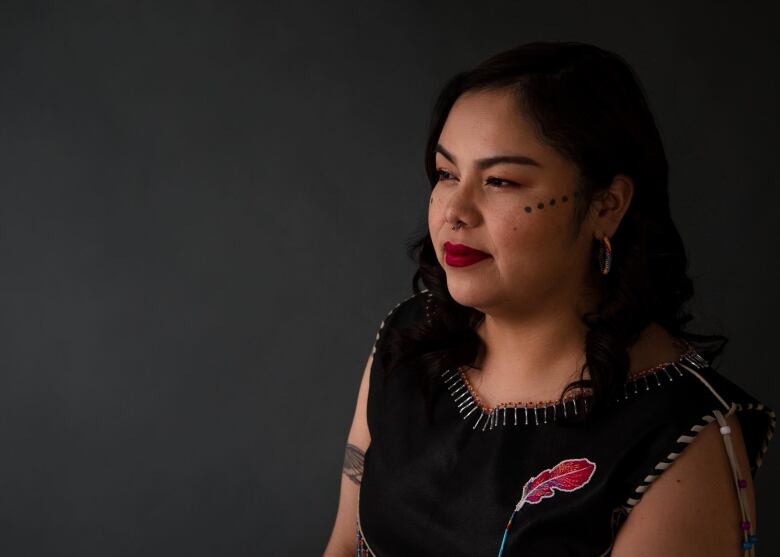 A two-spirit Indigenous person sitting in a black traditional regalia. 