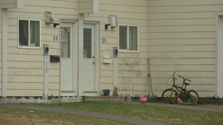 A run down yellow house with dirty siding and two doors.