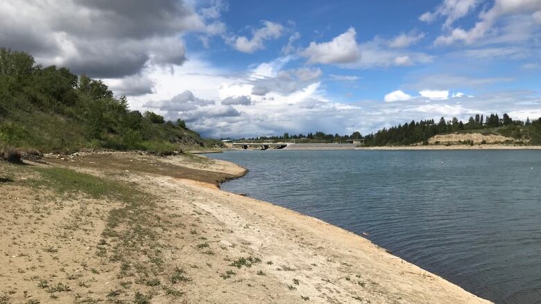 A snapshot of the Glenmore Reservoir and barren land next to the water.